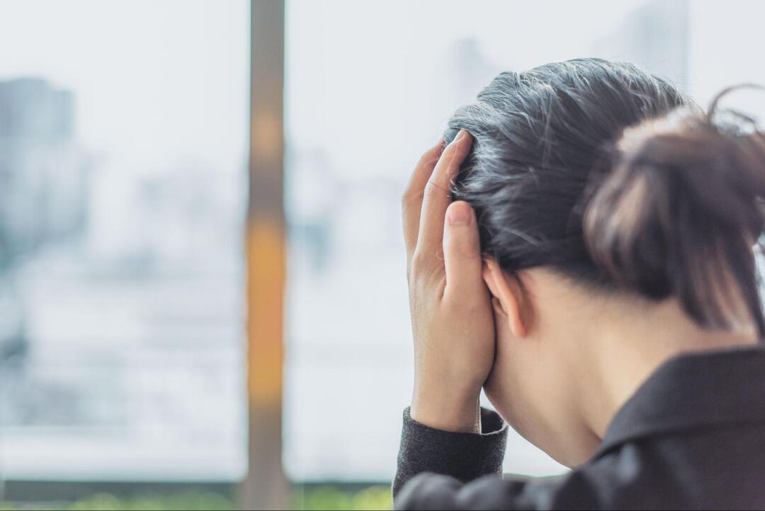両手で頭を抱えるようにして頭痛や強いストレスに耐えている、人物の後ろ姿