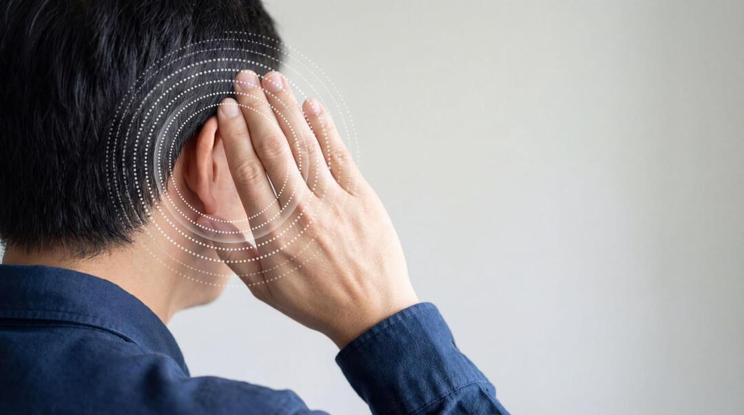 後ろ向きの男性が右耳に手を当て、耳を中心に音や耳鳴りをイメージさせる白い波紋のグラフィックが重ねられている
