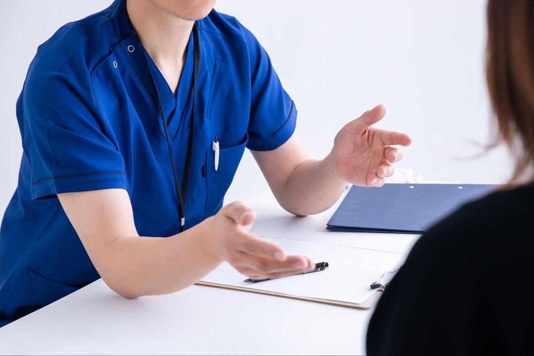 青いスクラブを着た医師が、患者に向けて両手を広げながら説明をしている様子