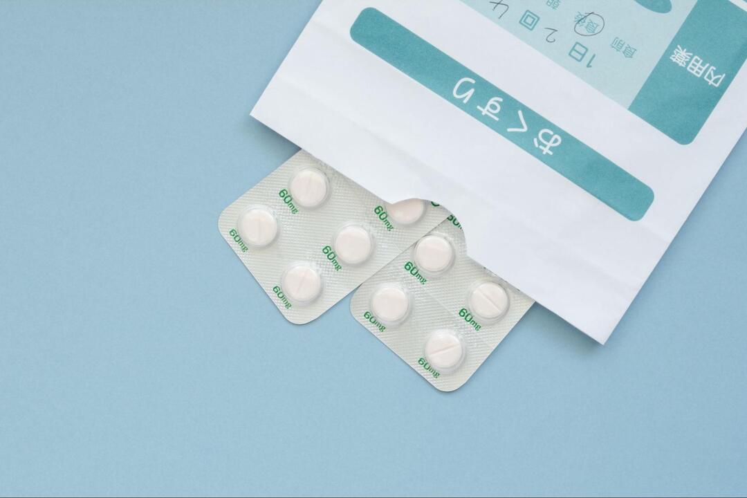 「おくすり」と書かれた調剤薬局の袋と、そこから半分覗いている白い錠剤のPTPシート2枚