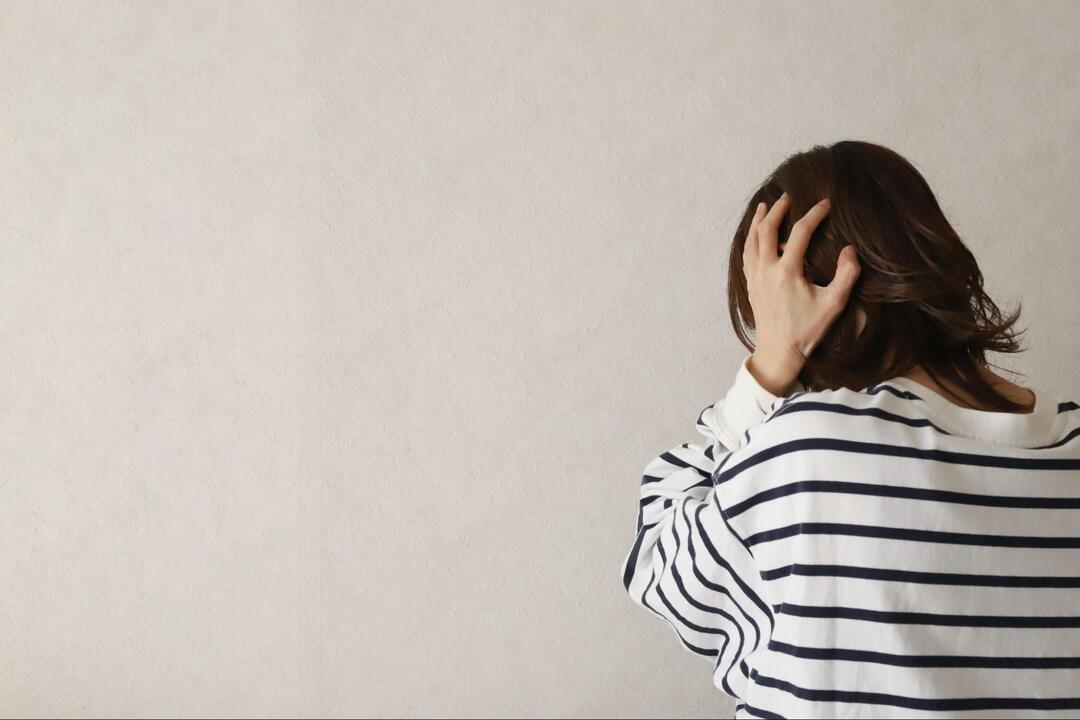 後ろ向きの女性が左手で頭を抱え込んでいる様子