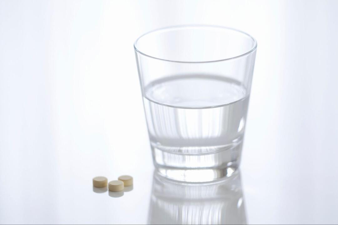 水が入ったグラスと、その手前に並ぶ3粒の小さな丸い錠剤
