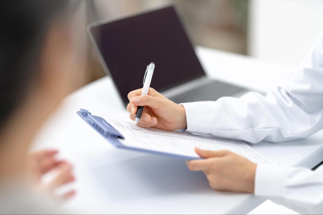 白衣を着た医師が、手元のバインダーに挟まれた書類にペンで記入している様子
