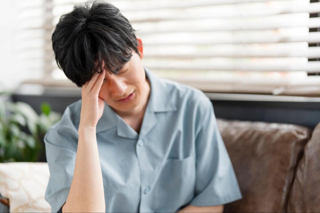 男性が目を閉じ、右手で額を抑えながら頭痛や体調不良に耐えている様子