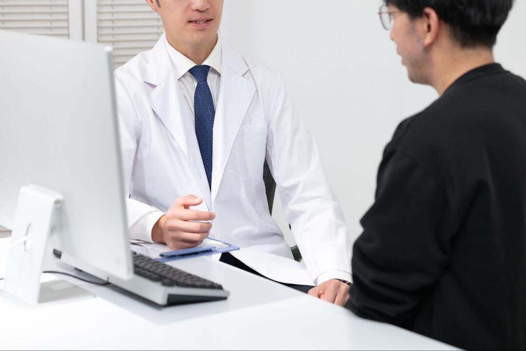 医師が診察室のデスクに座り、男性患者に向けて説明を行っている様子