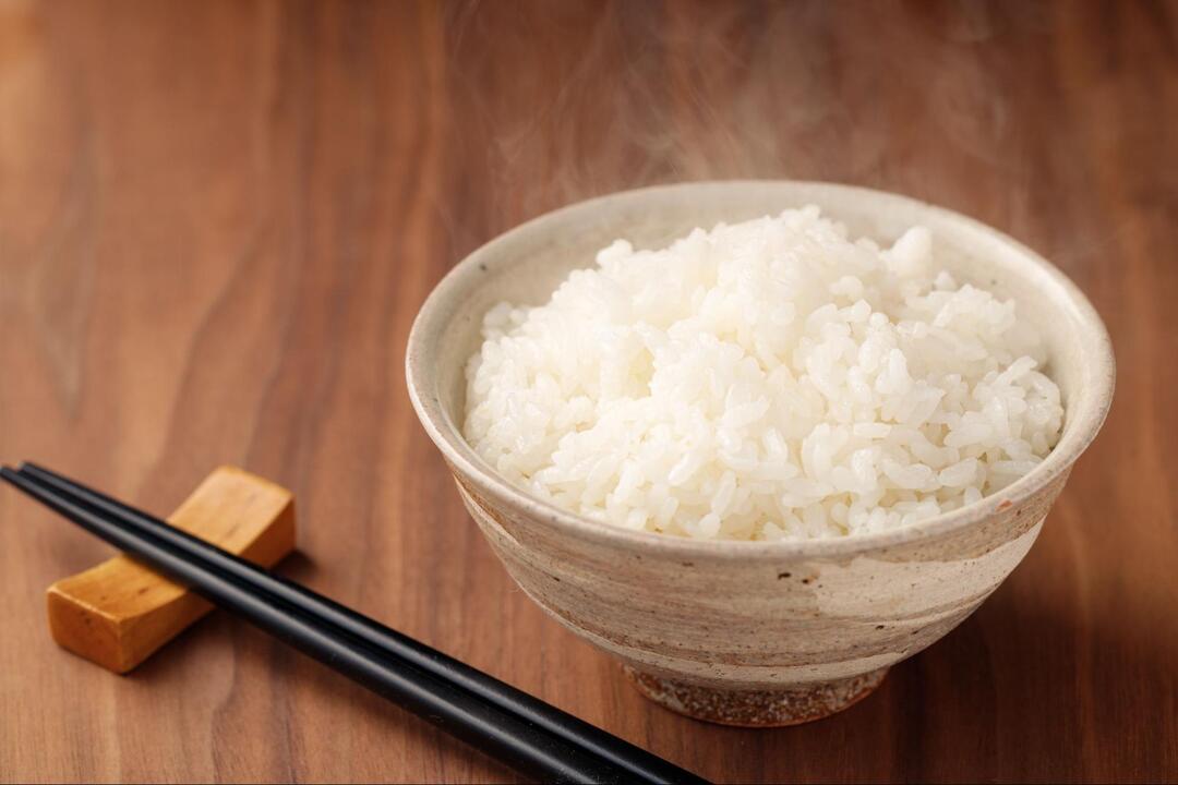 テーブルの上に置かれた湯気が立ち上るお茶碗一杯の白米と黒い箸