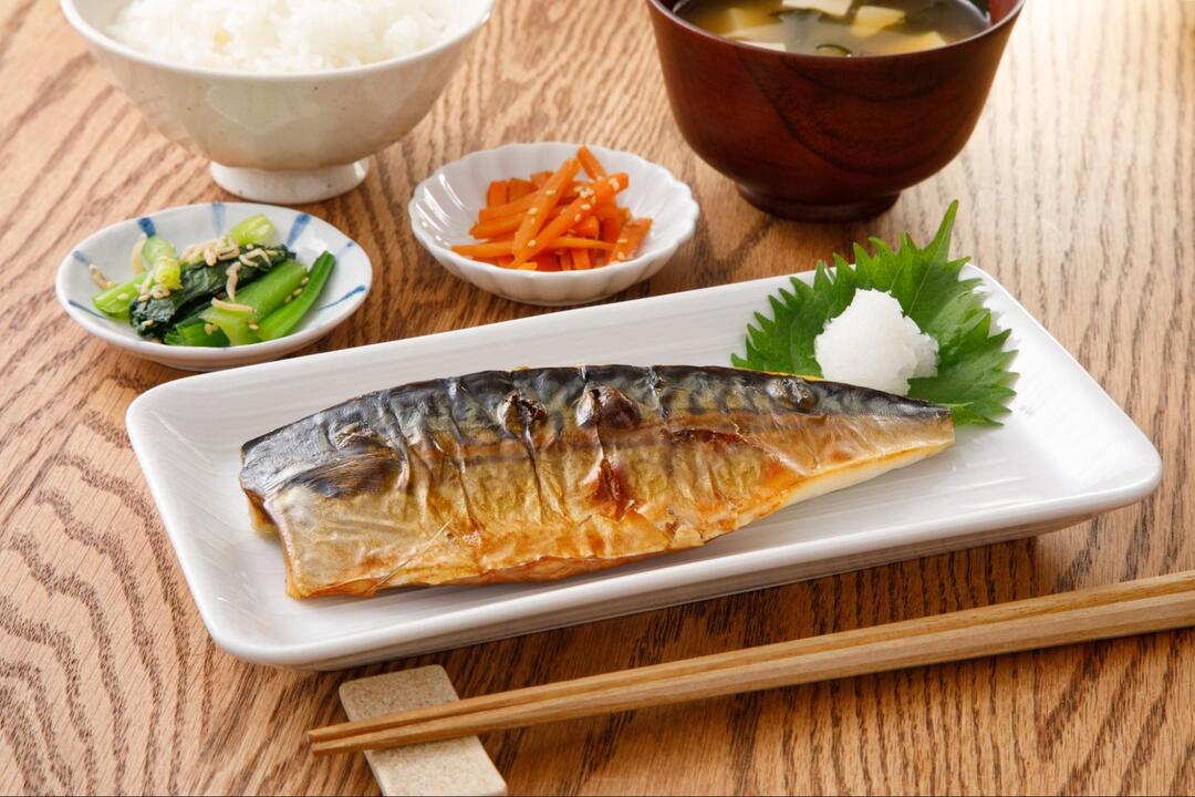 テーブルに並べられた魚の塩焼き、白米、味噌汁、2種類の小鉢からなる和食の定食