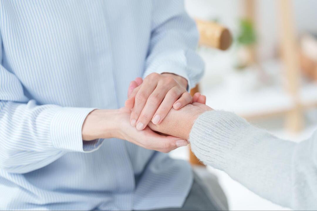水色のストライプシャツを着た人物が、グレーの服を着た人の手を優しく両手で包み込むように握っている手元のアップ